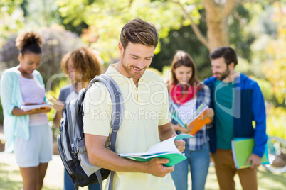 College boy reading notes with friends in background