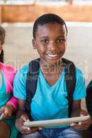 Smiling schoolboy using digital tablet at school