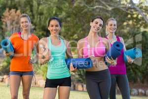 Beautiful women holding exercise-mat and bottle in park