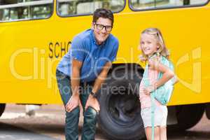 Smiling teacher and schoolgirl standing in front of school bus