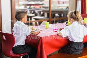 Boy and girl in school uniforms having lunch in school cafeteria