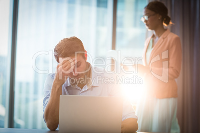 Frustrated businessman sitting on desk with hand on head