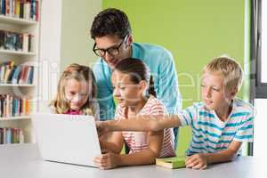 Teacher and kids using laptop in library