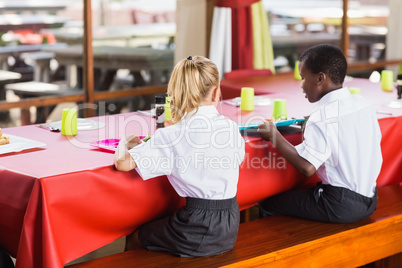 Boy and girl in school uniforms having lunch in school cafeteria