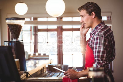 Waiter talking on mobile phone while using digital tablet