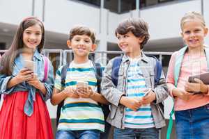 Kids holding mobile phone and digital tablet standing on school