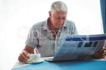 Retired man reading the news while holding a cup of tea