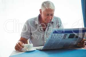Retired man reading the news while holding a cup of tea