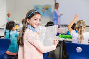 Portrait of schoolgirl standing with book in classroom