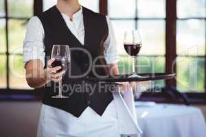 Mid section of waitress offering a glass of red wine