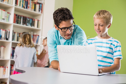 Teacher and schoolboy using laptop in library