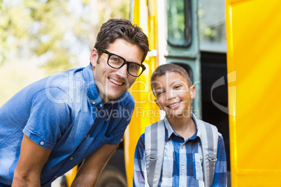 Smiling teacher and schoolboy standing in front of school bus