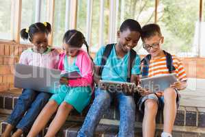 Kids sitting on staircase using laptop and digital tablet