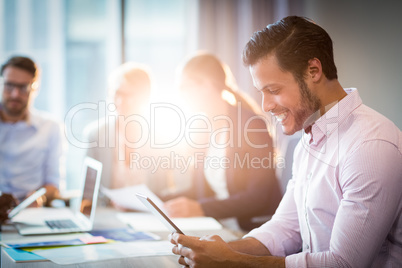 Man using digital tablet while coworker interacting in the backg