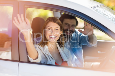 Happy couple waving hands while in car