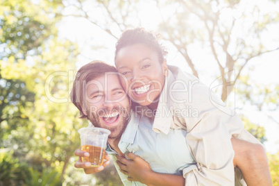 Man giving piggyback to woman while having glass of beer