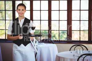 Smiling waitress holding a tray with glasses of red wine