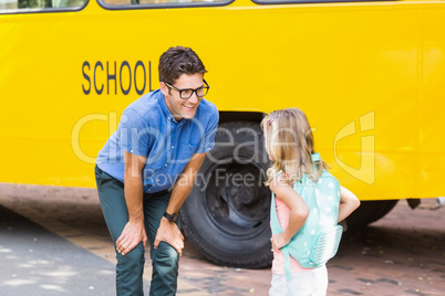 Teacher and schoolgirl interacting in front of school bus