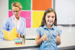 Schoolgirl showing thumbs up in classroom