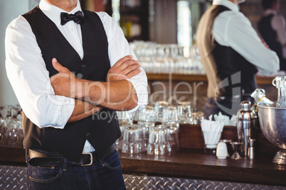 Mid section of bartender standing with arms crossed