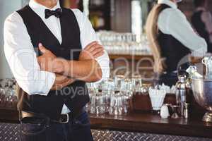 Mid section of bartender standing with arms crossed