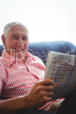 Senior man seated on a sofa looking at camera while holding news