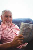 Senior man seated on a sofa looking at camera while holding news