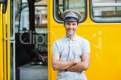 Smiling bus driver standing with arms crossed in front of bus