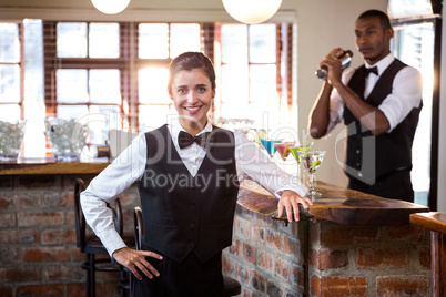 Smiling female bartender standing at bar counter