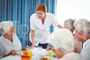 Smiling nurse looking at senior person during breakfast