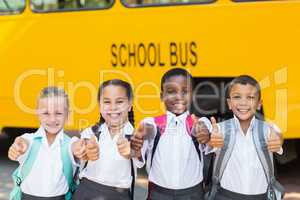 Smiling kids showing thumbs up in front of school bus