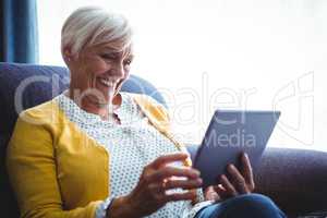 Smiling senior woman looking and laughing at her digital tablet