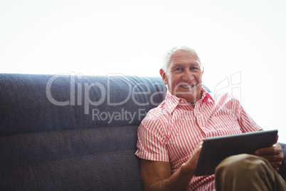 Senior man seated on a sofa while holding digital tablet