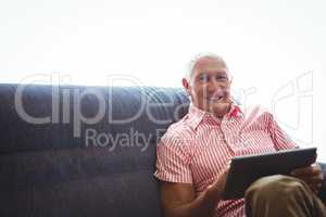 Senior man seated on a sofa while holding digital tablet