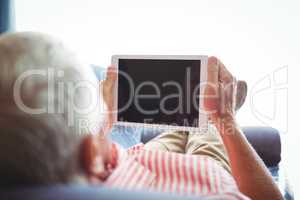 Lying on a couch senior man looking at digital tablet