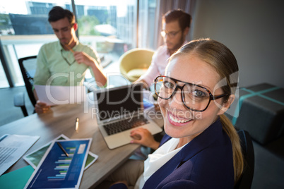 Businesswoman smiling at camera while her colleagues reading doc
