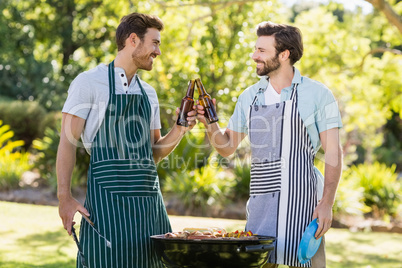 Men toasting beer bottle while preparing barbecue grill