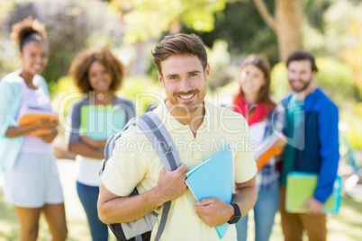 Portrait of college boy holding notes with friends in background