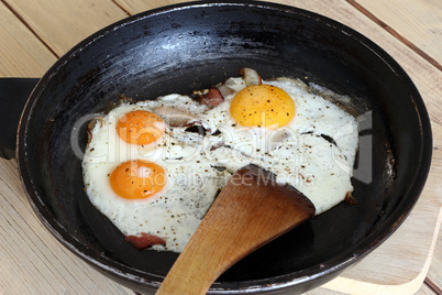 Fried eggs with bacon on the pan -  hearty breakfast