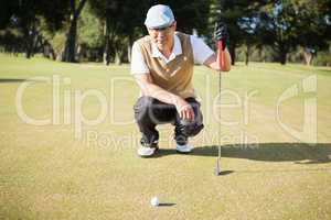 Golfer crouching and looking his ball