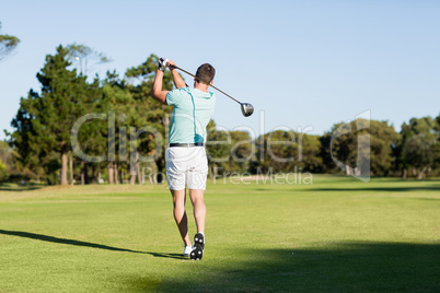 Rear view of young golfer man taking shot
