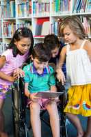 Handicapped boy holding digital tablet with friends at library