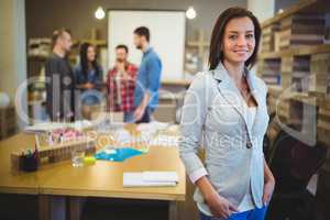 Confident young businesswoman standing by table
