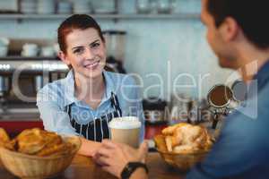 Portrait of happy barista giving coffee to customer at cafe