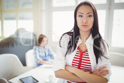 Confident young businesswoman with colleague in background at of