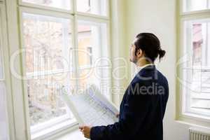 Interior designer with blueprint looking though window