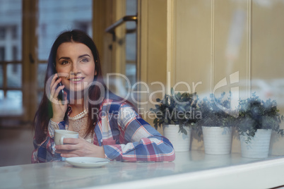 Happy woman listening to mobile phone at cafe
