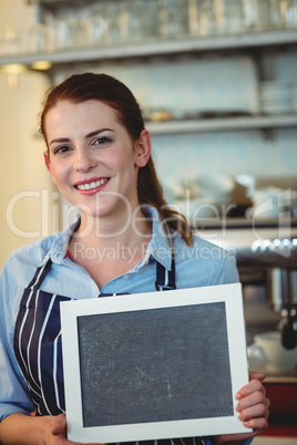 Portrait of confident barista holding blank blackboard at cafe
