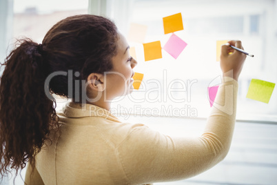 Rear view of businesswoman writing on adhesive notes office