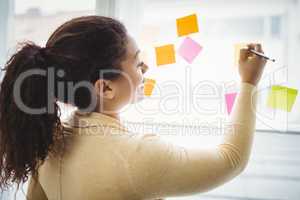 Rear view of businesswoman writing on adhesive notes office